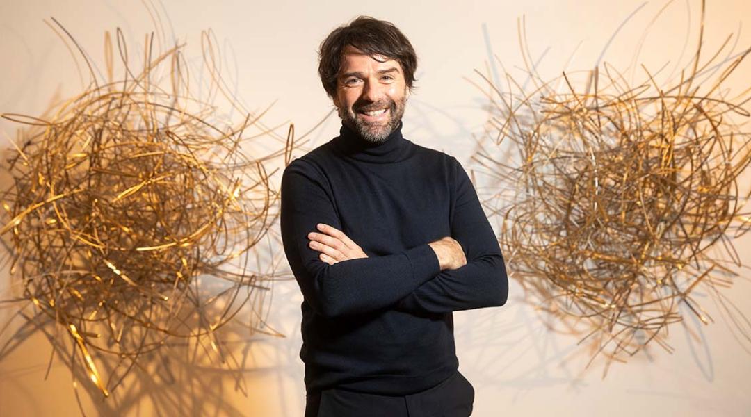 Sculptor David Rodríguez Caballero poses smiling next to one of his works